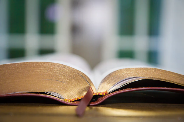 Close-up of an open book with golden-edged pages resting on a textured green English fabric background.