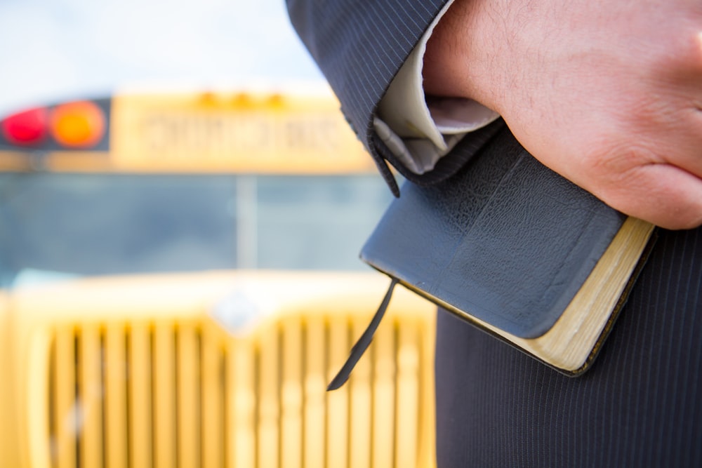 a close up of a person holding a book in front of a school bus