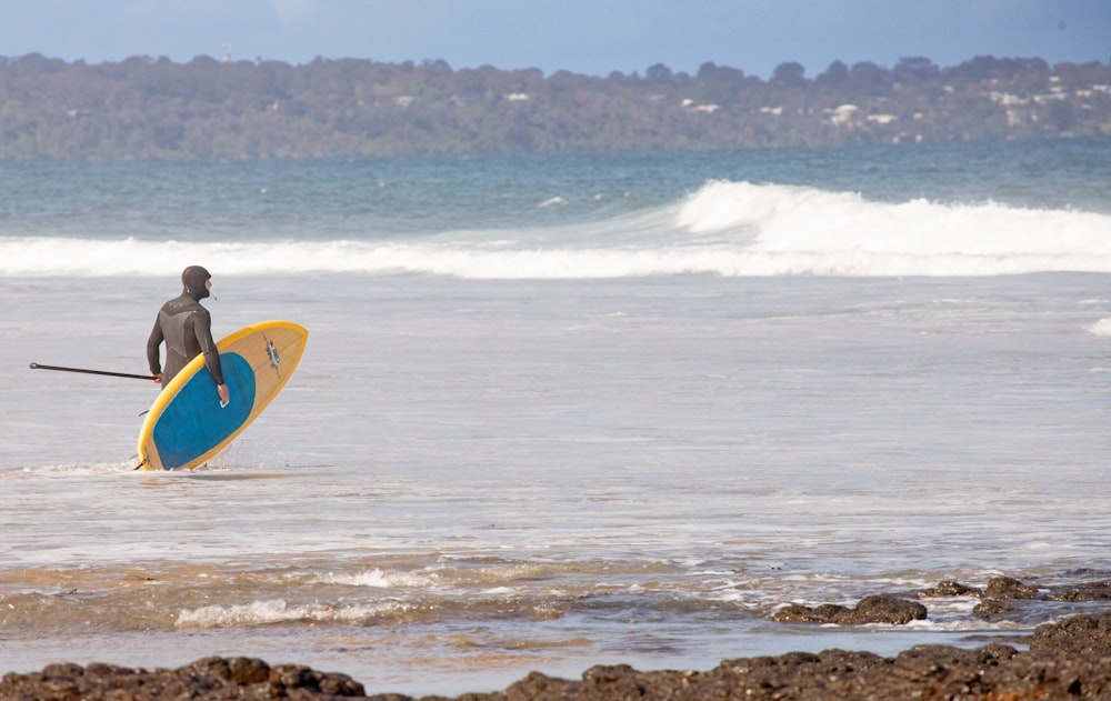 Un homme tenant une planche de surf debout dans l’océan