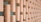 A series of vertically oriented, light-colored wooden blocks arranged in a staggered, grid-like pattern. Each block is connected to the next by thin horizontal rods, creating a three-dimensional effect. The backdrop is a muted green wall, providing contrast to the wood texture.