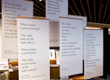 Several large posters are hung in a room, each displaying quotes from Bob Dylan. The quotes cover topics like creativity, life experiences, and personal reflection. The room has a modern design with visible wooden elements on the ceiling and a few pieces of furniture and books in the background.