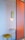 A minimalist interior setting with a small wooden table attached to a vibrant orange partition. A yellow wall lamp with a circular design illuminates the space softly. A yellow cushioned stool with light blue legs is placed under the table.