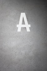 A large white letter 'A' is prominently displayed on a speckled gray concrete surface. The background is dotted with small dark green and black specks.