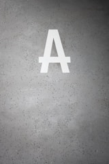 A large white letter 'A' is prominently displayed on a speckled gray concrete surface. The background is dotted with small dark green and black specks.