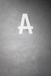 A large white letter 'A' is prominently displayed on a speckled gray concrete surface. The background is dotted with small dark green and black specks.