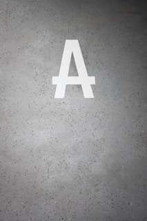 A large white letter 'A' is prominently displayed on a speckled gray concrete surface. The background is dotted with small dark green and black specks.