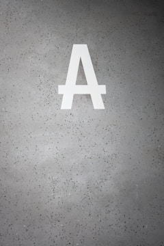 A large white letter 'A' is prominently displayed on a speckled gray concrete surface. The background is dotted with small dark green and black specks.