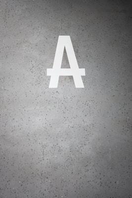 A large white letter 'A' is prominently displayed on a speckled gray concrete surface. The background is dotted with small dark green and black specks.
