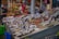A busy fish market stall displaying a variety of fresh seafood including fish and shrimp on ice. The setup includes yellow price tags, and there are blurred figures of people in the background, indicating a lively market atmosphere.