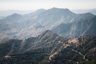 A scenic view of a winding mountain road surrounded by lush greenery and distant peaks.