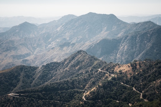 A scenic view of a winding mountain road surrounded by lush greenery and distant peaks.