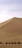 A group of travelers riding camels across golden desert dunes under a clear blue sky.