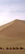 A group of travelers riding camels across golden desert dunes under a clear blue sky.
