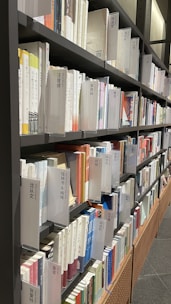 Books neatly arranged on metal shelves, prominently displaying visible Chinese characters on the spines. The setting appears to be a library or a bookstore. The shelves are filled with books of various colors and thicknesses, creating an orderly and structured appearance.