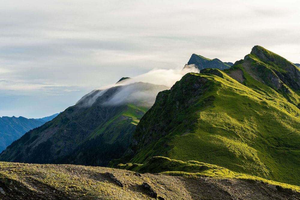 a green mountain with a few clouds in the sky