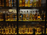 A dimly lit shelf lined with vintage genever bottles glowing softly under warm, golden light.