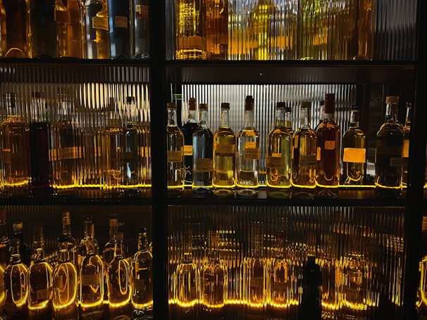 Vibrant neon-lit bottles of fernet lined up on a dark shelf.