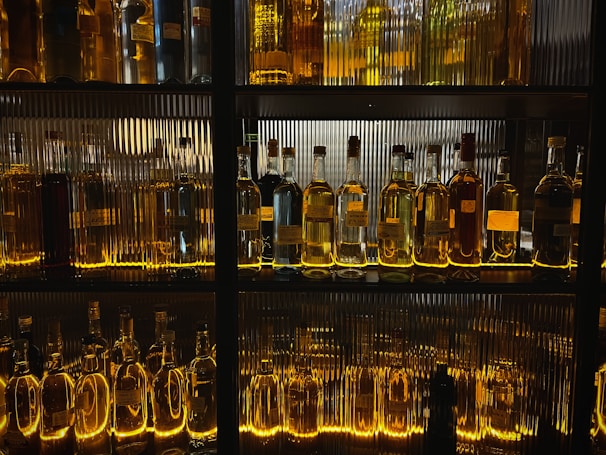 A sleek row of premium liquor bottles illuminated softly, showcasing rich labels and gold accents.