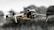 A quadcopter drone in flight, featuring four propellers attached to a sleek, metallic body. The camera at the front is prominently visible, and the background is slightly blurred with natural elements, suggesting it is outdoors.