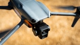A close-up view of a modern drone capturing detailed design features such as the camera and wing structure. The background is blurred, highlighting the drone's sleek, aerodynamic body.