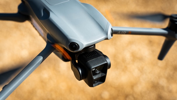 A close-up view of a modern drone capturing detailed design features such as the camera and wing structure. The background is blurred, highlighting the drone's sleek, aerodynamic body.