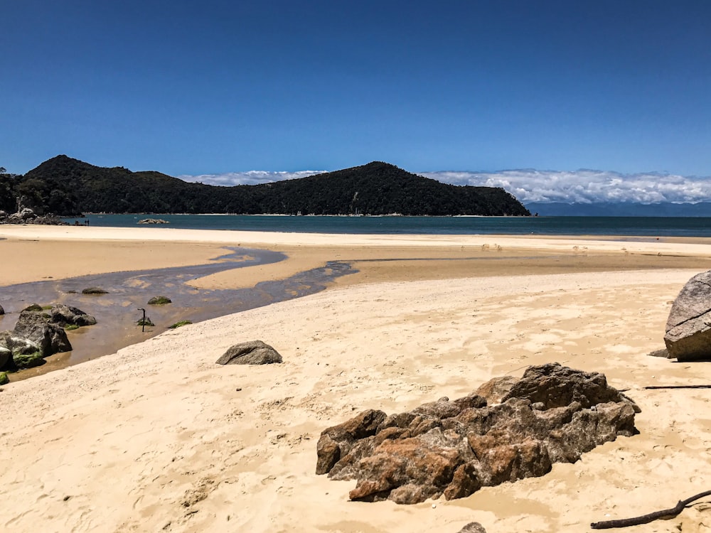 uma praia de areia com uma grande rocha em primeiro plano