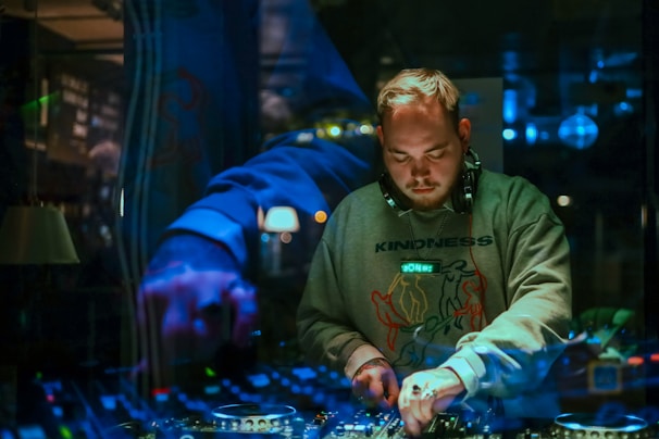 Lynnie E behind the DJ booth, headphones on, focused on mixing tracks live.