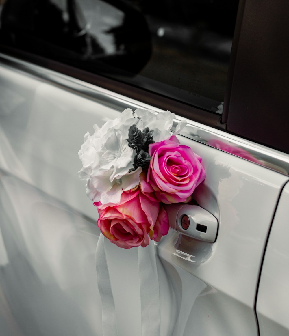 um buquê de rosas cor-de-rosa sentado ao lado de um carro branco