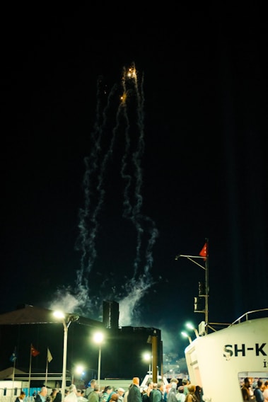 Crowd celebrating with fireworks lighting up the night sky over Olbia's harbor.