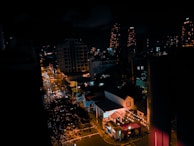 A nighttime cityscape showing a well-lit event venue with people arriving.