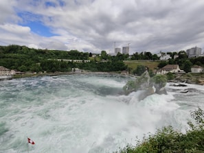 A panoramic view of a Swiss waterfall surrounded by lush greenery.