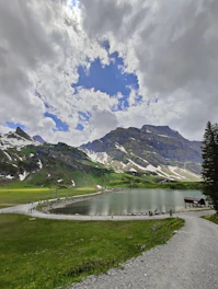 A serene mountain landscape with travelers exploring a winding trail under a clear blue sky.