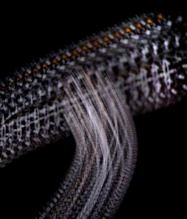 An abstract pattern featuring interwoven lines and textures, with a dark background. The intricate design includes repeating geometric shapes with hints of orange, set against a combination of white and dark tones.