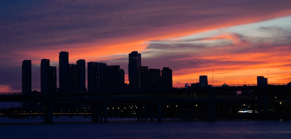 a sunset view of a city with a bridge in the foreground