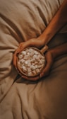 a person holding a bowl of marshmallows on a bed
