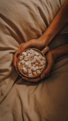 a person holding a bowl of marshmallows on a bed