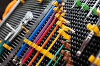 A collection of neatly organized hand tools, including wrenches and screwdrivers, is arranged on a perforated panel. The tools have colorful handles in shades of yellow, blue, red, and purple, which are secured in position by yellow fasteners. The background pattern is composed of a series of black circular holes, adding a textured look to the arrangement.