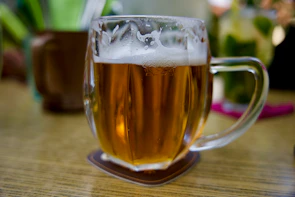 Close-up of a traditional ceramic beer mug filled with frothy beer on a rustic bar counter.