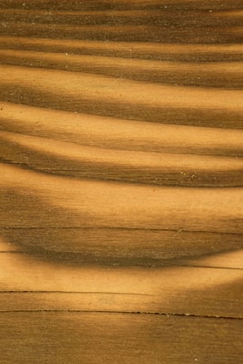 Close-up view of a wooden surface with natural grain patterns running horizontally across. The surface appears to be smooth with a slight texture, highlighting the natural variations in the wood.