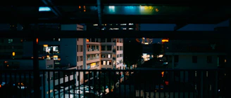 Cinematic night view from a penthouse balcony overlooking city lights with soft gold accents and an elegant crowd blurred in the background.