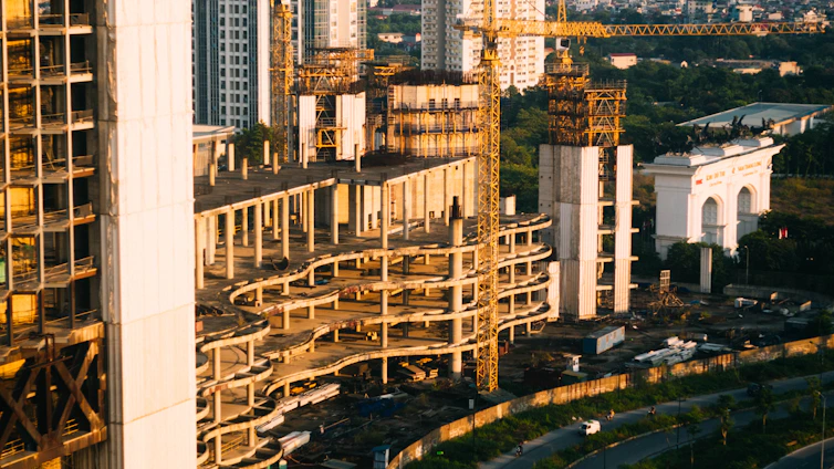 A sleek modern construction site at sunset with cranes and a partially completed luxury villa in the background.