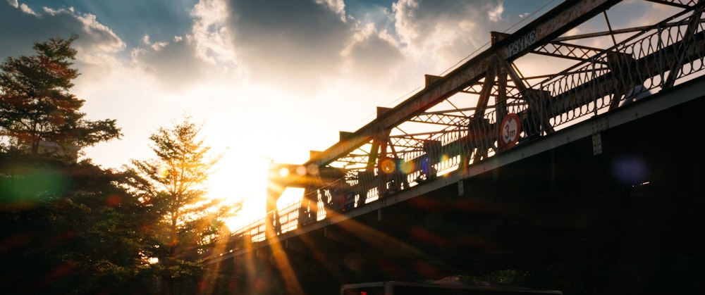 the sun is setting over a bridge and trees