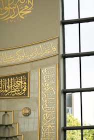 Close-up of intricate Islamic calligraphy wall art framed in soft gold on a pristine white wall.
