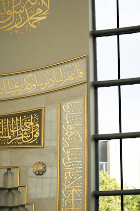 Elegant emerald green wall adorned with a large qurb calligraphy piece framed in metallic gold, capturing light beautifully.