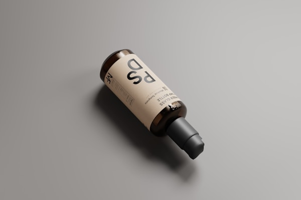 A brown bottle with a black pump dispenser lies on a flat surface, featuring a minimalist label with bold, stylized text. The bottle is positioned diagonally across a muted background, creating a clean and modern aesthetic.