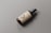 A dark brown glass bottle with a pump dispenser lies on a matte gray surface. The bottle is labeled with large letters 'PSD' and smaller text at the top and bottom. The label is a light beige color.