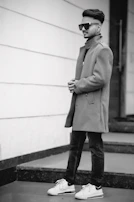 A model walking confidently down a city street wearing a sharp, tailored coat paired with casual sneakers.