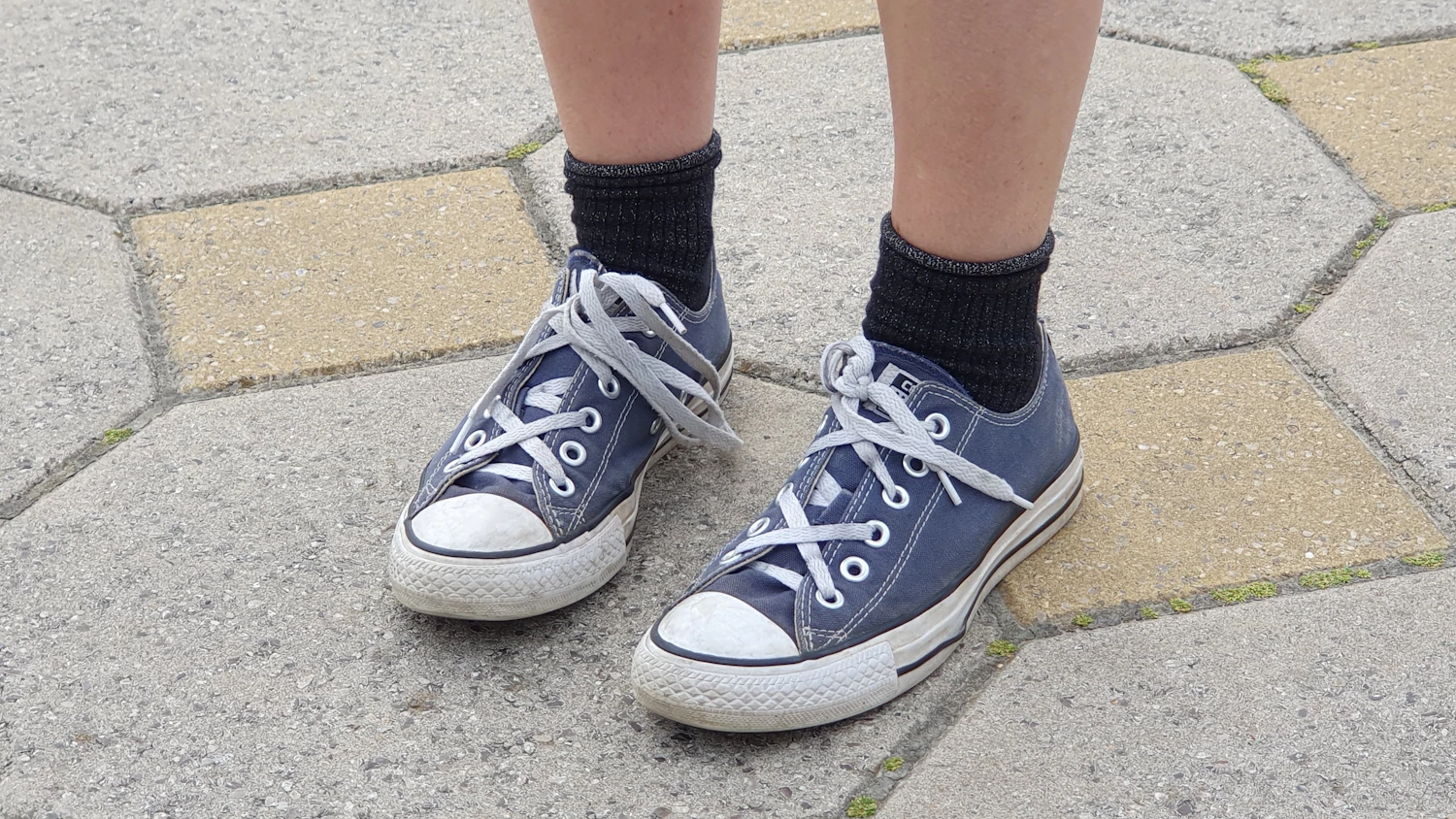 Child wearing blue lace-up sneakers on a paved path