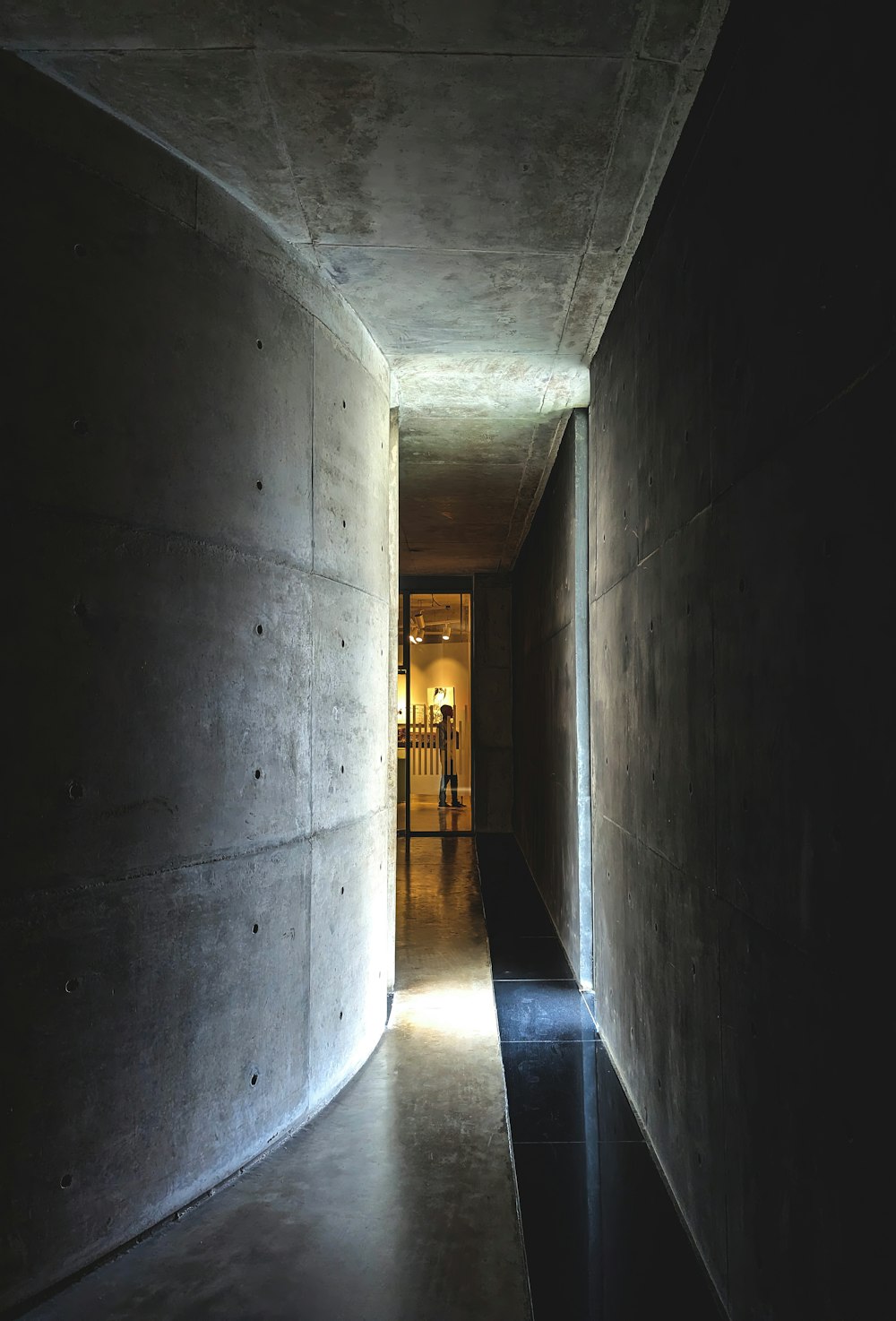 a long hallway with concrete walls and a light at the end