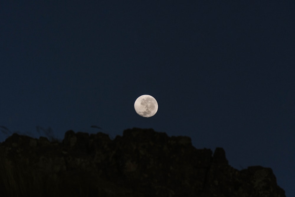 a full moon is seen in the sky above a mountain